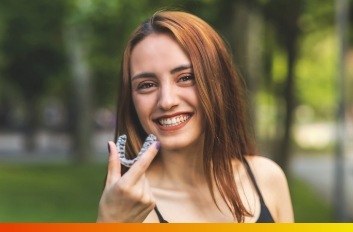 Smiling young woman holding Invisalign clear aligner