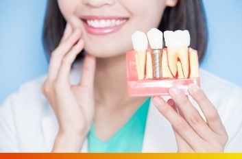 Dentist touching their jaw while holding a dental implant model