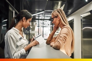 Woman showing a pamphlet to woman across desk from her