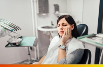 Woman in dental chair holding her jaw in pain
