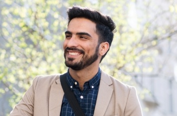 Man in beige dinner jacket smiling with trees in background