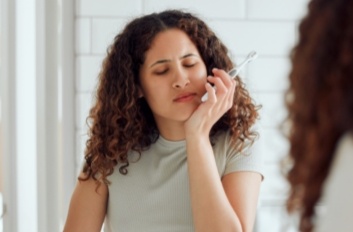 Woman with toothbrush holding her jaw in pain