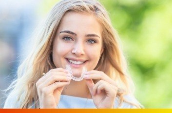 Smiling young woman holding Invisalign clear aligner