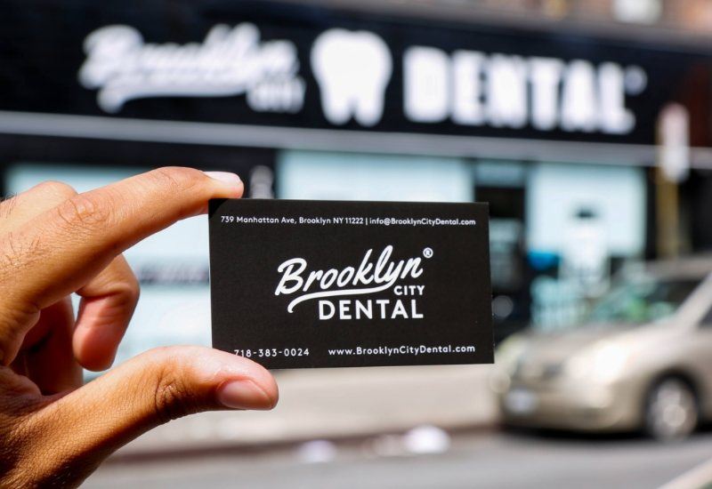 Person holding Brooklyn City Dental business card in front of the dental office