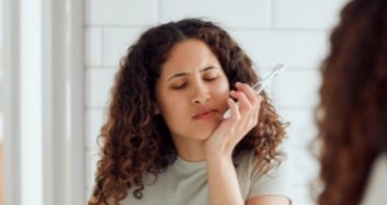 Woman with toothbrush holding her jaw in pain