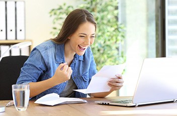 Woman celebrating at her desk while looking at dental insurance