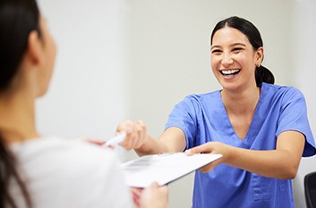 Dental assistant smiling while handing patient form