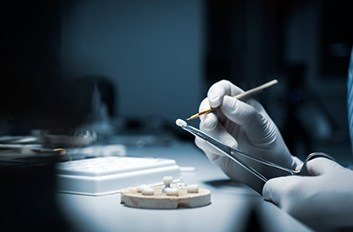 A person wearing gloves carefully sculpts a dental prosthetic with a brush and tool.